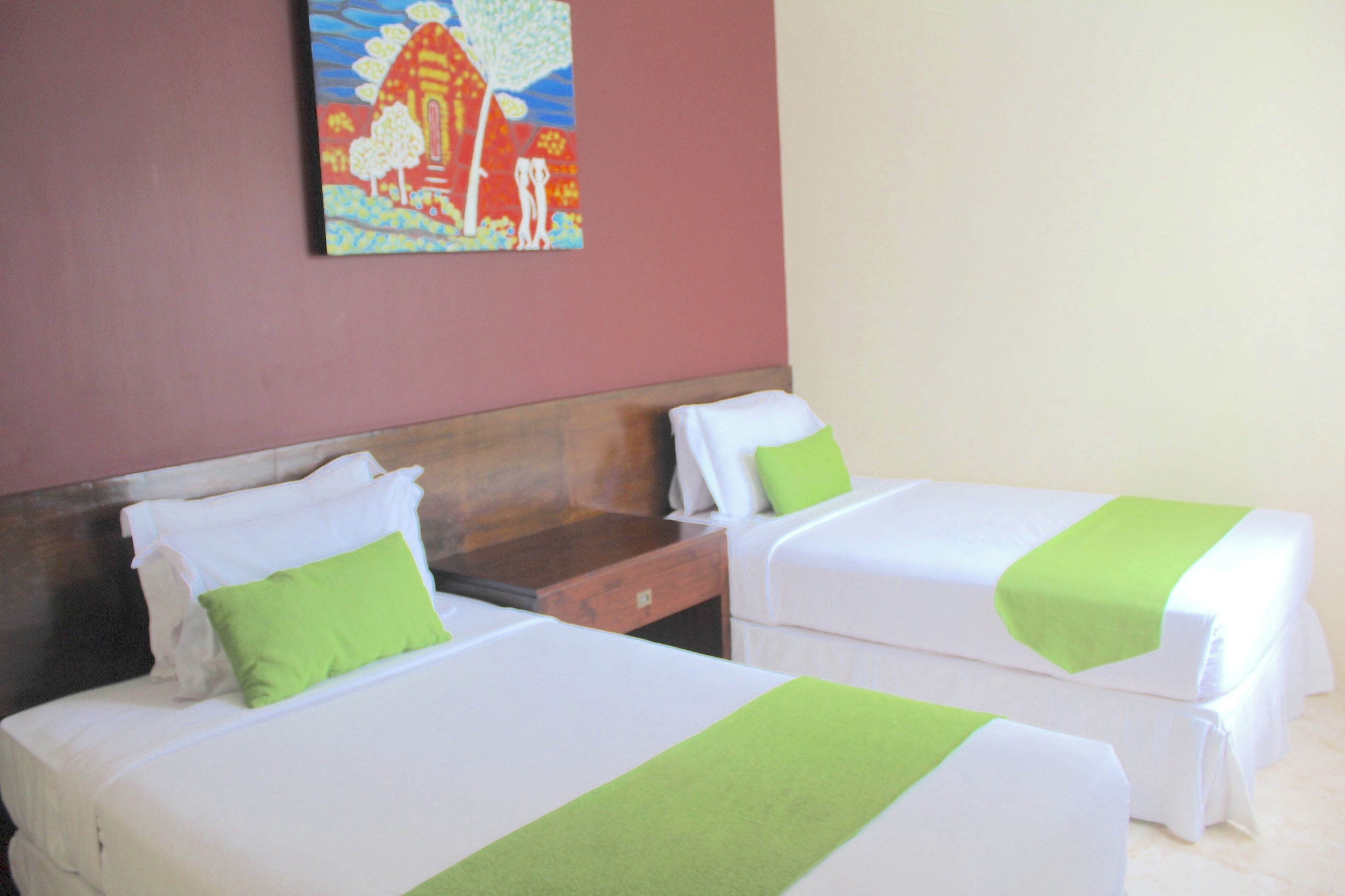 Two beds with white linens and green accents, a wooden headboard, and a painting on the wall.