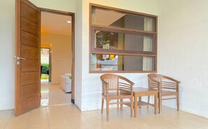 A room with a wooden door, a large window, and two wooden chairs.