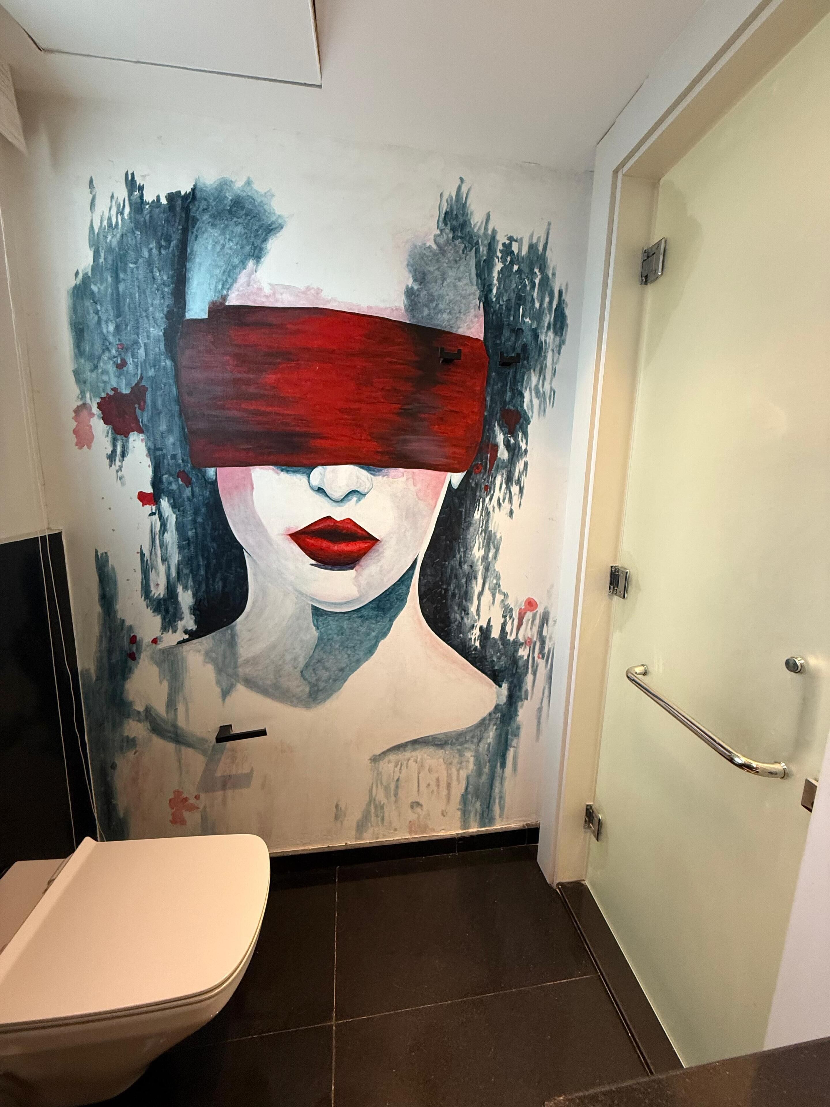 A bathroom with a large mural on the wall, a white bathtub, and a door with a handrail.