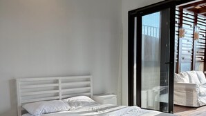 A modern bedroom with a white bed, wooden flooring, and a large sliding glass door leading to a balcony. - ALSAWAH Modern Rooftop with Private Terrace Sheikh Zayed (Sheikh Zayed City)