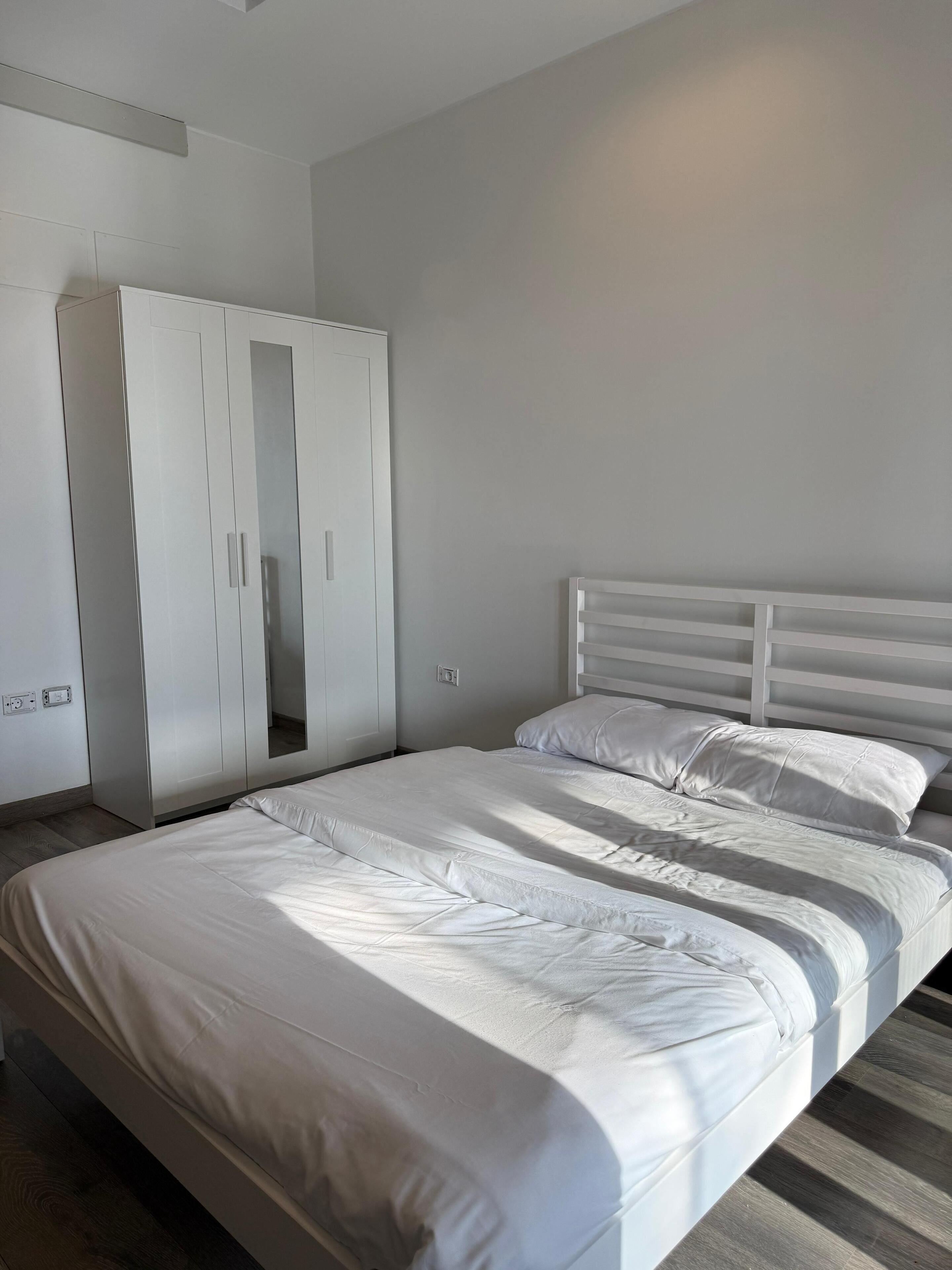 A bedroom with a bed, white headboard, and a wardrobe with a mirror.