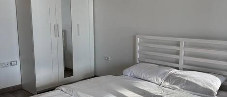 A bedroom with a bed, white headboard, and a wardrobe with a mirror.