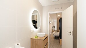 Une salle de bain moderne avec un miroir rond, un meuble-lavabo en bois, un lavabo et des toilettes.