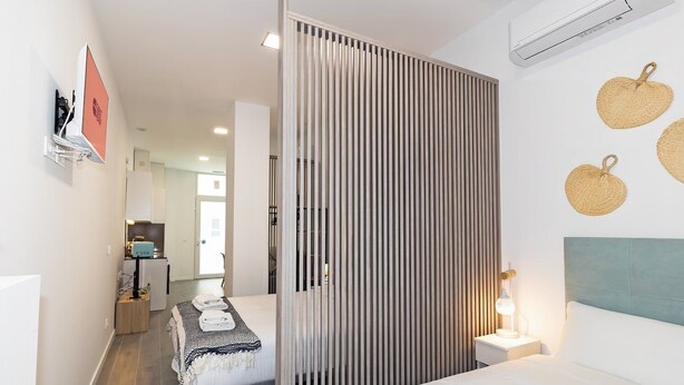 Une chambre d’hôtel moderne, équipée d’un lit, d’une table de chevet et offrant une vue sur le couloir.