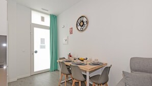 Un coin repas avec une table en bois, quatre chaises grises et une horloge murale.