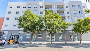 Un bâtiment moderne à plusieurs étages, doté de fenêtres numérotées et de balcons, d’une aire de stationnement avec un chariot élévateur, et sous un ciel dégagé.