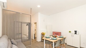 Une pièce moderne et minimaliste comprenant un coin repas avec une table en bois et des chaises grises, un canapé gris et un meuble blanc contenant une machine à café.