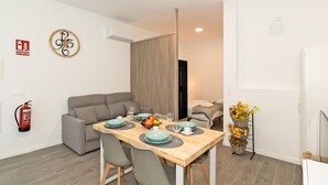 Un espace repas moderne avec une table en bois dressée pour quatre personnes, un canapé gris et une petite table d’appoint sur laquelle est posé un vase de fleurs.