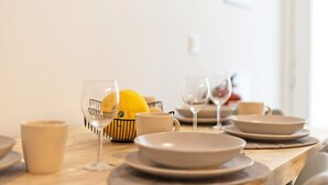 Een eettafel gedekt met borden, kommen en glazen, met een citroen in een draadmandenmand.