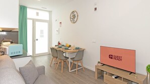 Un soggiorno moderno con un divano, un'area pranzo con tavolo e sedie, un televisore su un mobile e una cucina con un forno a microonde.