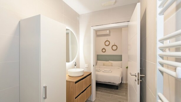 Een moderne badkamer met een rond wastafel, een houten opbergmeubel en een bed met hoofdbord.