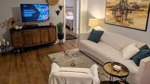 Un salon avec un téléviseur, un canapé blanc, une table basse et un tableau accroché au mur.