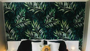 Un lit recouvert d’une couvre-lit à motifs, deux tables de chevet blanches avec des lampes, et un mur orné d’un motif végétal.