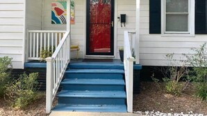 Une maison avec une porte rouge, une façade blanche et des marches bleues menant à un porche.