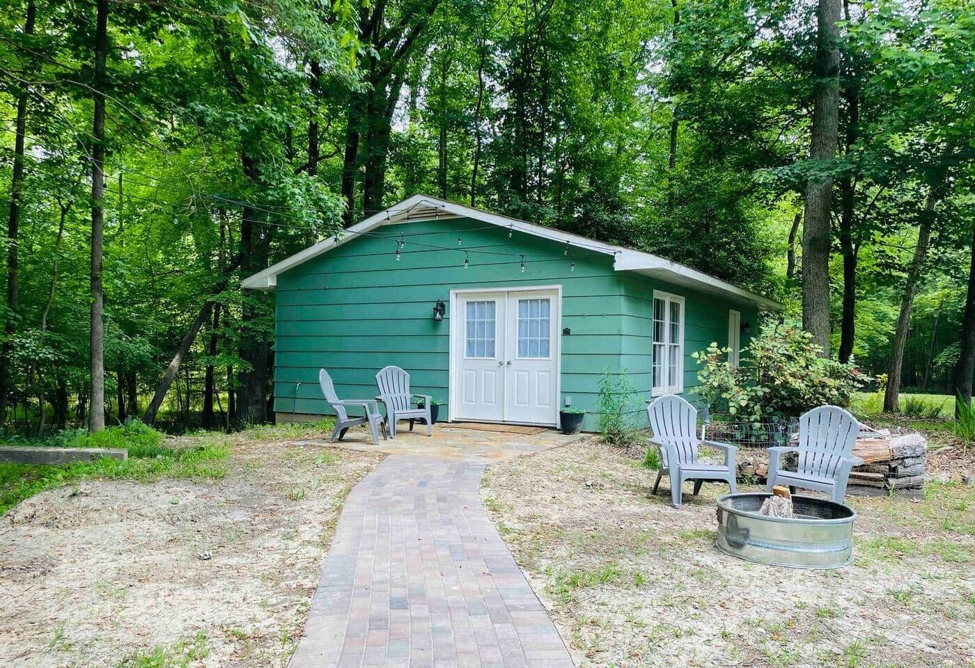 A green cabin with a brick pathway leading to it, surrounded by trees.