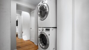 A laundry room with two stacked front-loading washing machines, wooden flooring, and white walls. - Contemporary City Getaway  Luxe Comfort (Arlington)