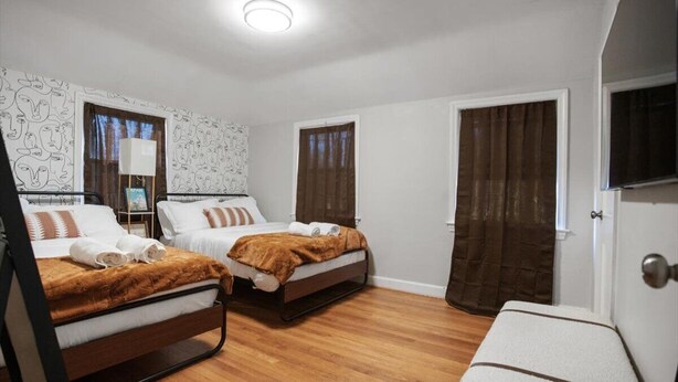 A hotel room with two beds, wooden flooring, a white wall with a pattern, and a door with a curtain. - Contemporary City Getaway  Luxe Comfort (Arlington)
