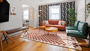 A living room with a brown leather sofa, a green armchair, a checkered rug, and a patterned wall. - Contemporary City Getaway  Luxe Comfort (Arlington)