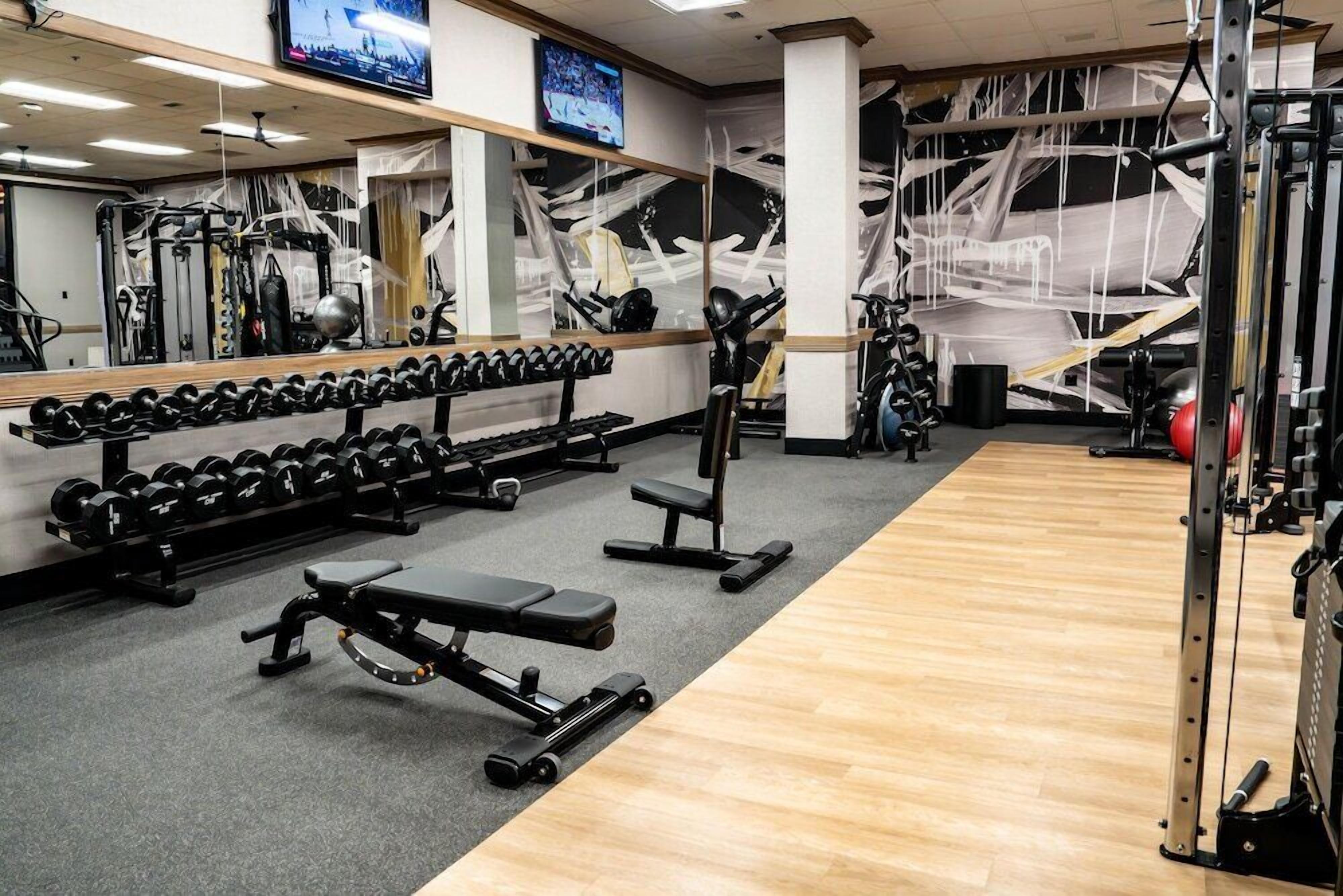 Une salle de sport équipée de matériel de musculation, de miroirs et d’un téléviseur.