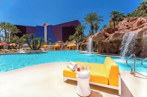Un espace piscine agrémenté d’une cascade, de chaises longues et de parasols.