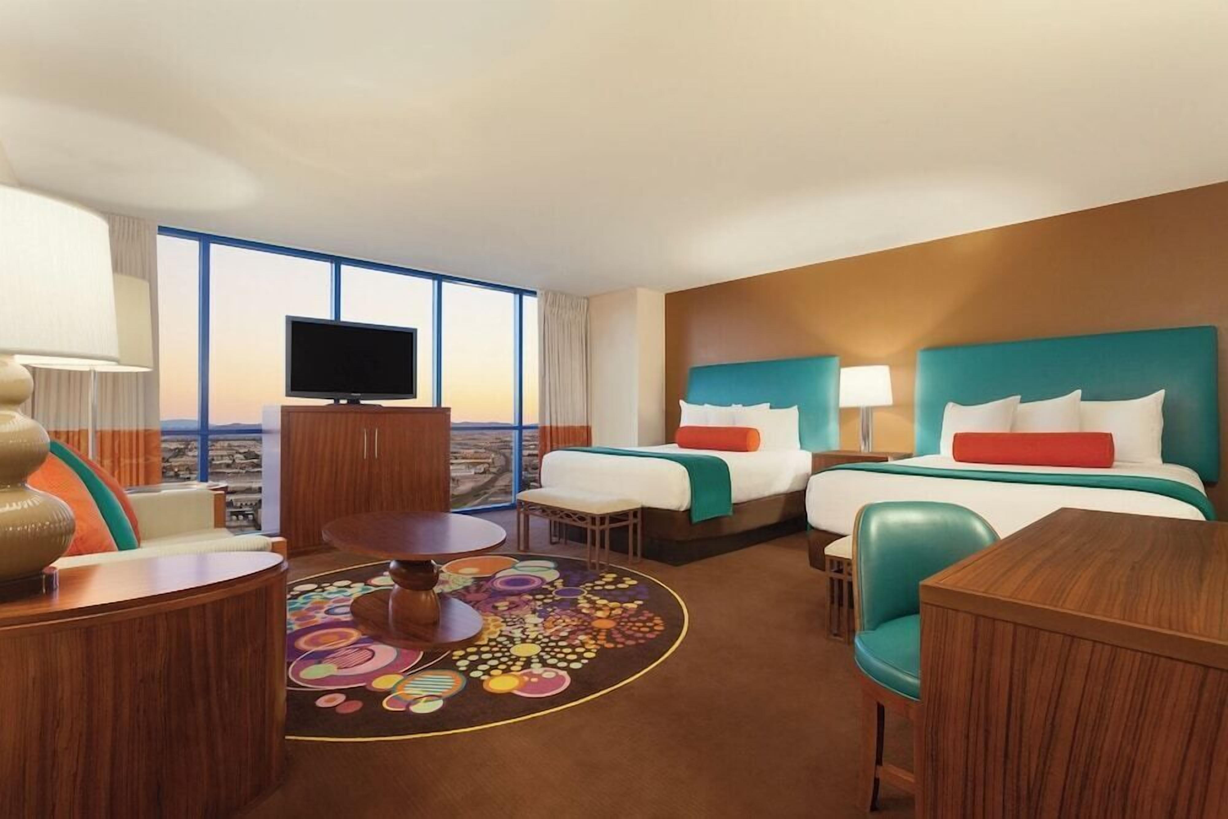 A hotel room with two beds, a TV, a desk, and a view of the city.