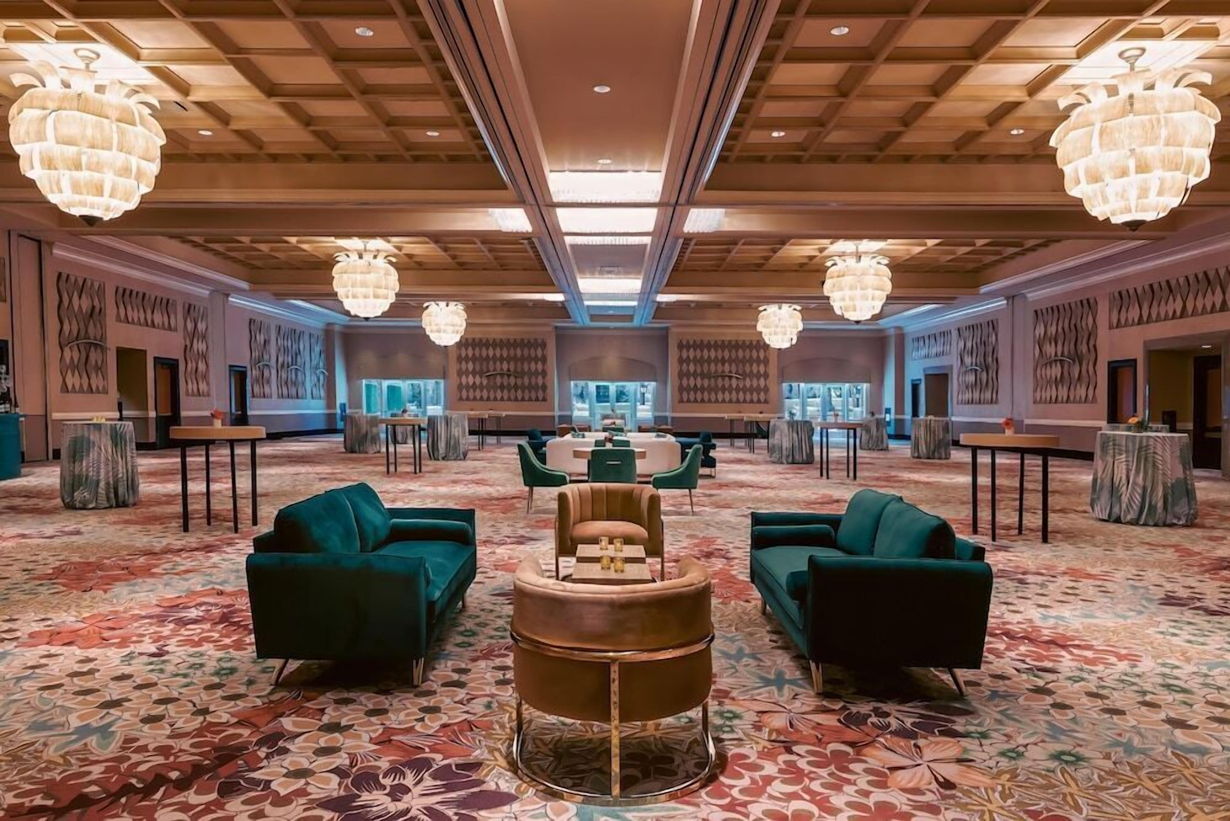 Un vestíbulo amplio con alfombra estampada, sofás verdes, una mesa central y candelabros decorativos.