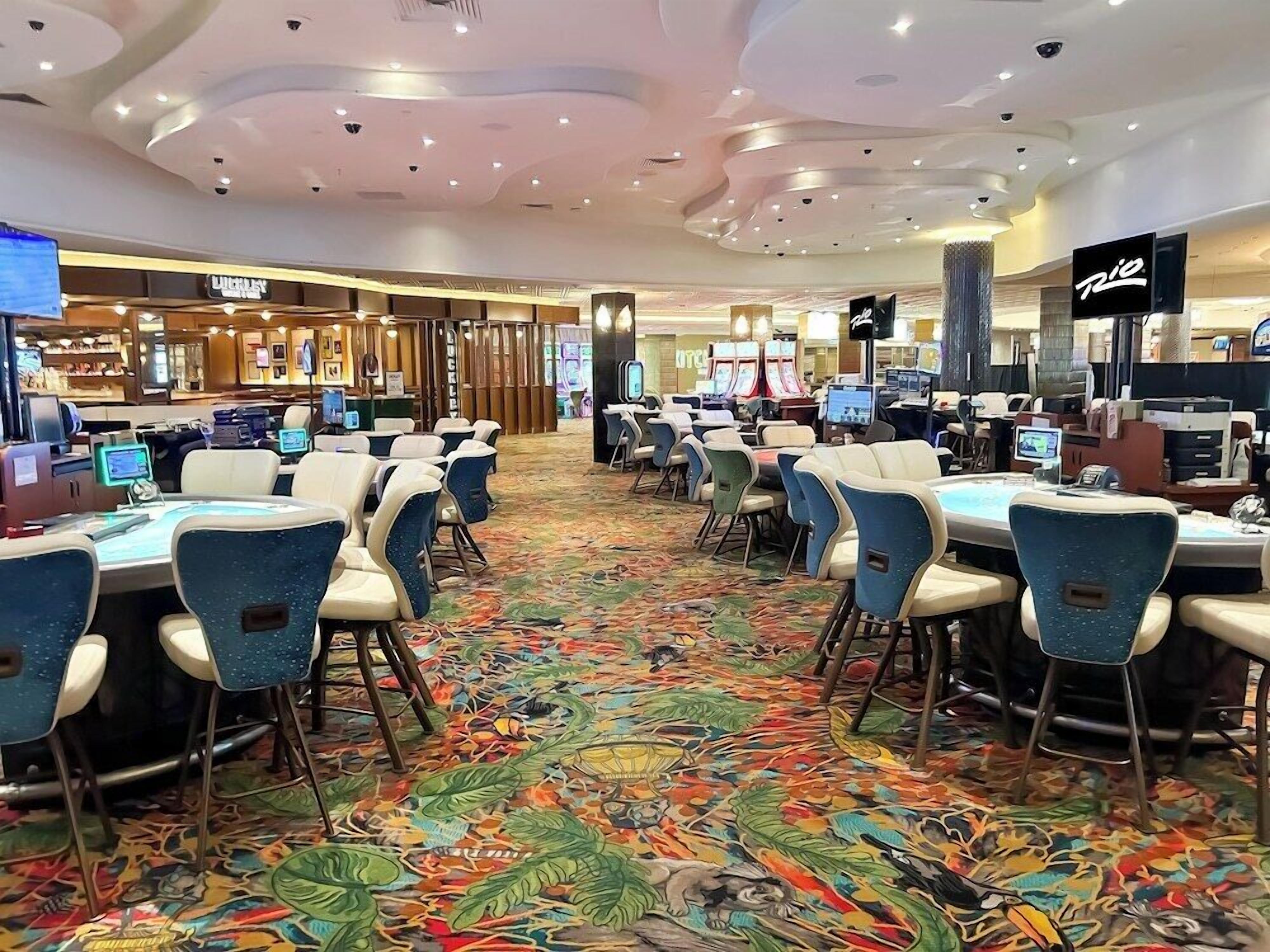 A hotel lobby with a colorful carpet, multiple gaming machines, and a 'Rio' sign.