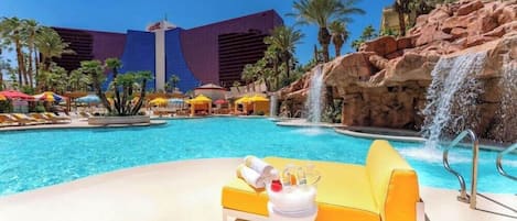 A pool area with a waterfall feature, lounge chairs, and umbrellas.