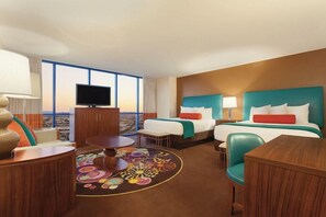 A hotel room with two beds, a TV, a desk, and a view of the city.