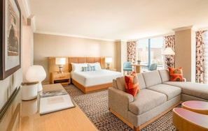 A hotel room with a bed, a sofa, a desk with a lamp, and a view of the city.