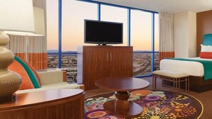 A hotel room with a large window, a television, a bed, a sofa, a small table, and a colorful rug. - 2 Connecting Suites at a  Hotel (Las Vegas)