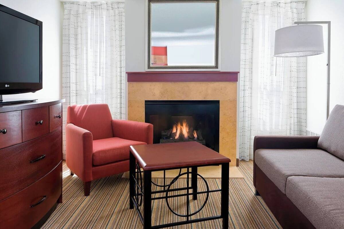 A hotel room with a TV, a fireplace, a red armchair, a brown sofa, and a table.