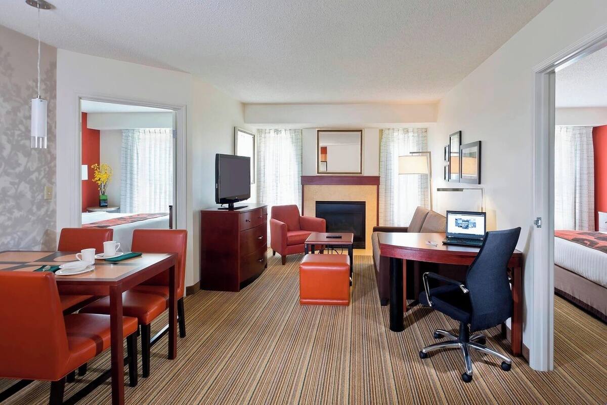 A hotel room with a dining area, a fireplace, a TV, and a bed.