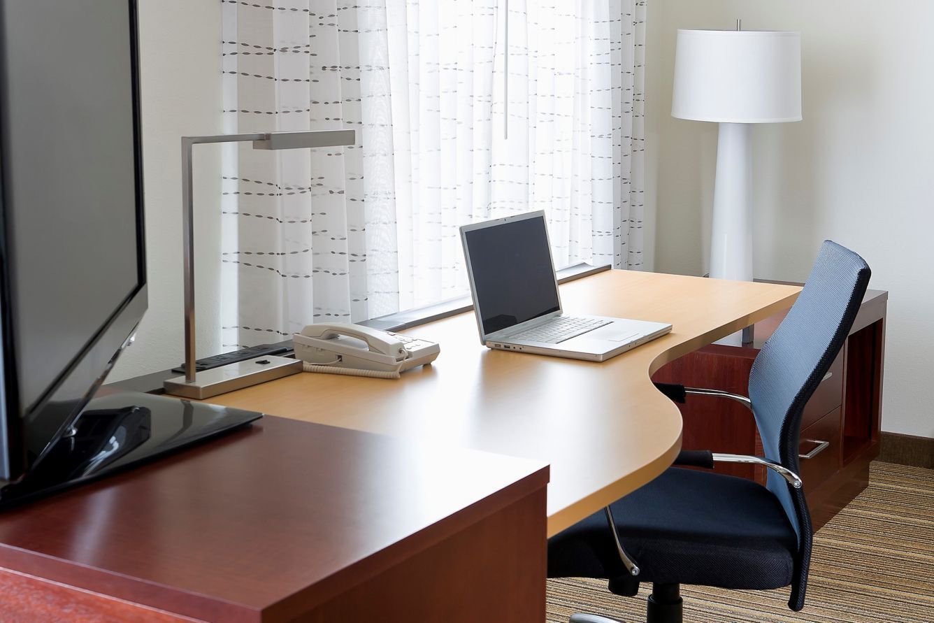 A hotel room with a desk, laptop, telephone, and a lamp.