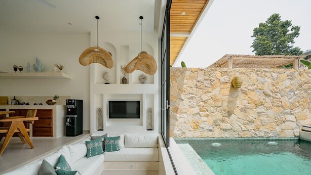 A modern living room with a stone wall, a pool, and a sofa with cushions. - Villa Maiora Tres Bingin (Pecatu)