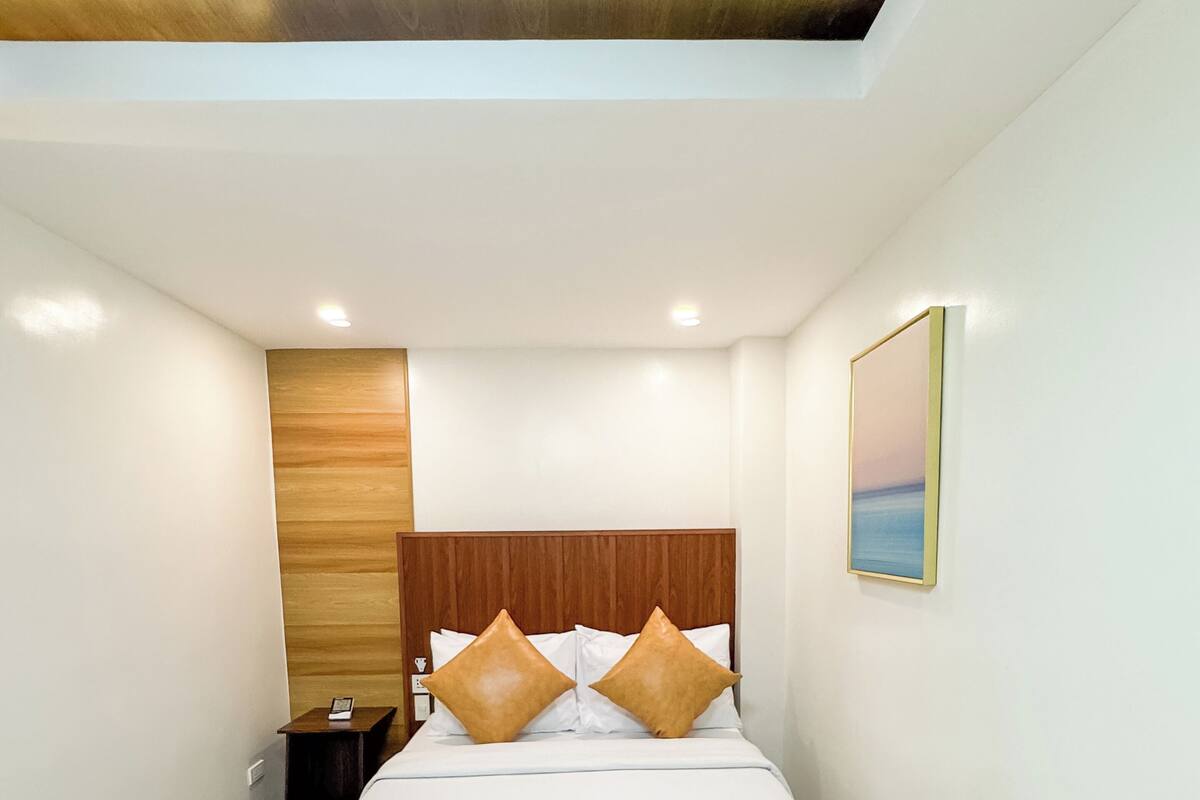 Ein modernes Hotelzimmer mit einem großen Bett, einem Holz-Kopfteil, einem Nachttisch und einem Bild an der Wand.