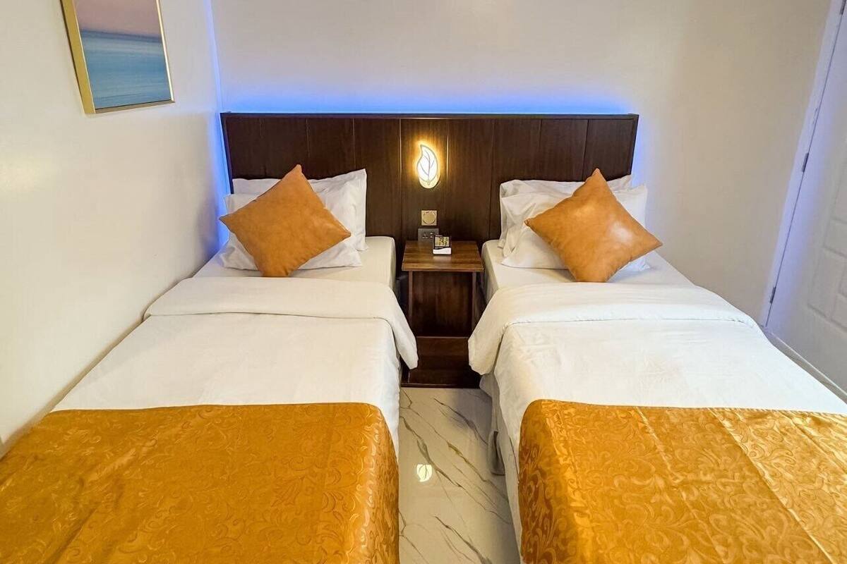 Ein Hotelzimmer mit zwei Betten, einem hölzernen Kopfteil, einem Nachttisch und einer Wandleuchte.