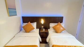 Une chambre d’hôtel avec deux lits, une tête de lit en bois, une table de chevet et un luminaire fixé au mur.