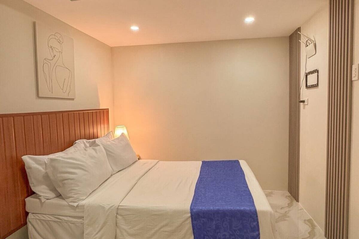 Ein Schlafzimmer mit einem Holz-Kopfteil, einem Bett mit weißer Bettwäsche und einer blauen Decke, einem Boden mit Marmor-Muster und einer Holzausschlag-Decke.