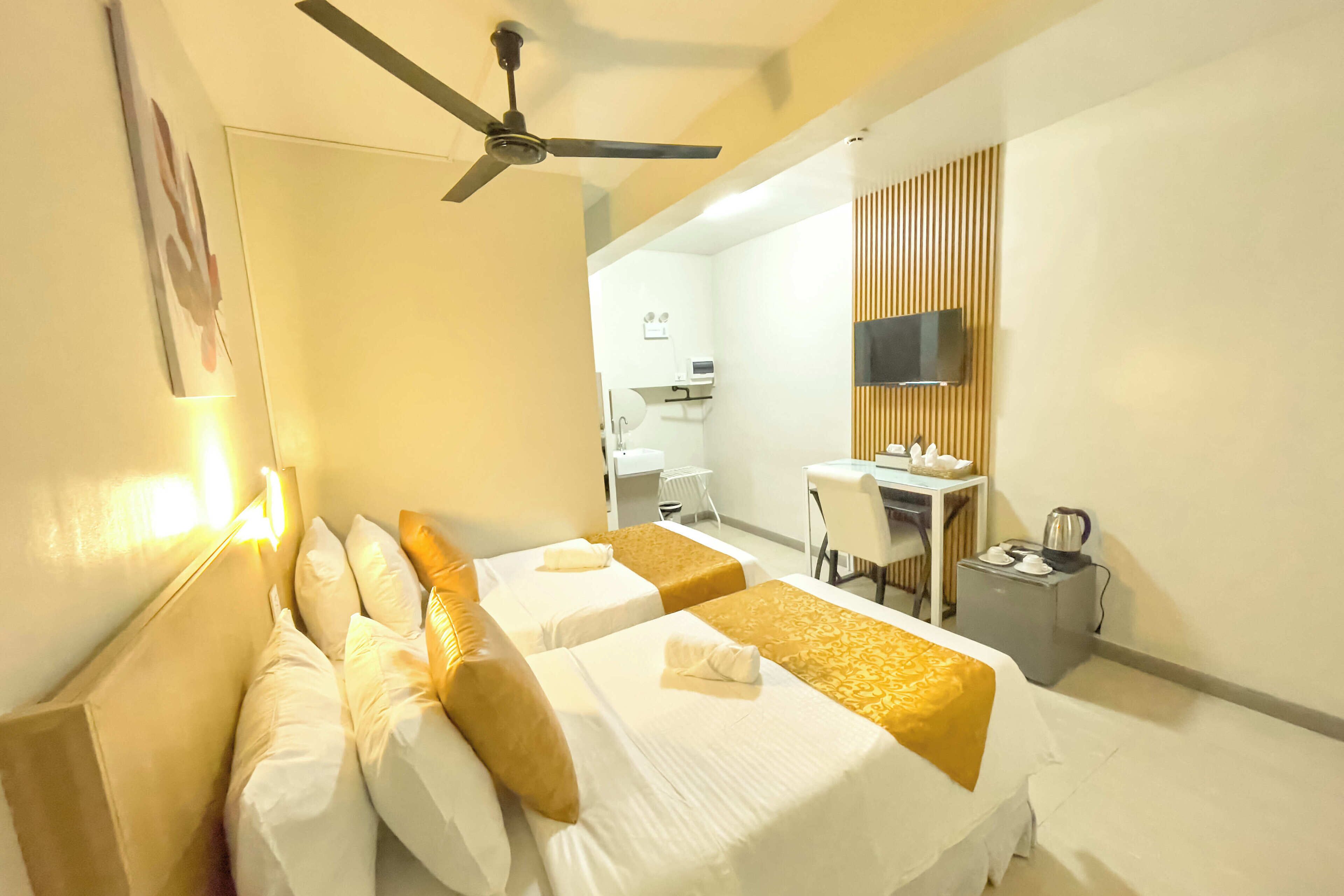 Habitación de hotel con dos camas, un escritorio, una silla, un televisor y un ventilador de techo.