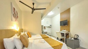 A hotel room with two beds, a desk, a television, and a kitchenette.