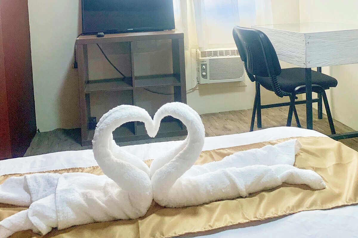 Habitación de hotel con cama, televisor sobre un mueble, una silla y aire acondicionado instalado en la pared.