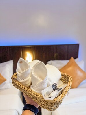 A hand holding a wicker basket with neatly folded white towels and a bottle of lotion. - Hotel Adelina Balanga City Bataan (Balanga)