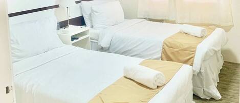 A hotel room with two beds, each with white linens and a beige bed runner. There is a nightstand with a lamp and a phone.