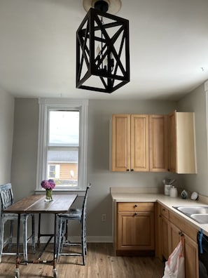 A kitchen with wooden cabinets, a dining table with chairs, a hanging light fixture, and a window with a view.