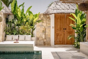 A poolside area with a stone wall, wooden door, and thatched roof structures. - MaÏa Villa Bingin (Pecatu)