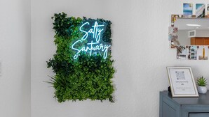 Een neonbord met de tekst 'Salty Sanctuary' op een muur, omringd door groene begroeiing.