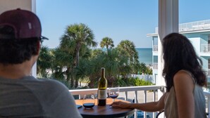 Een balkon met een tafel, een fles wijn en uitzicht op het strand en palmbomen.