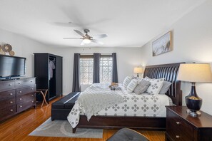 Ein Schlafzimmer mit Bett, Fernseher, Kleiderschrank, Schreibtisch und Deckenventilator.