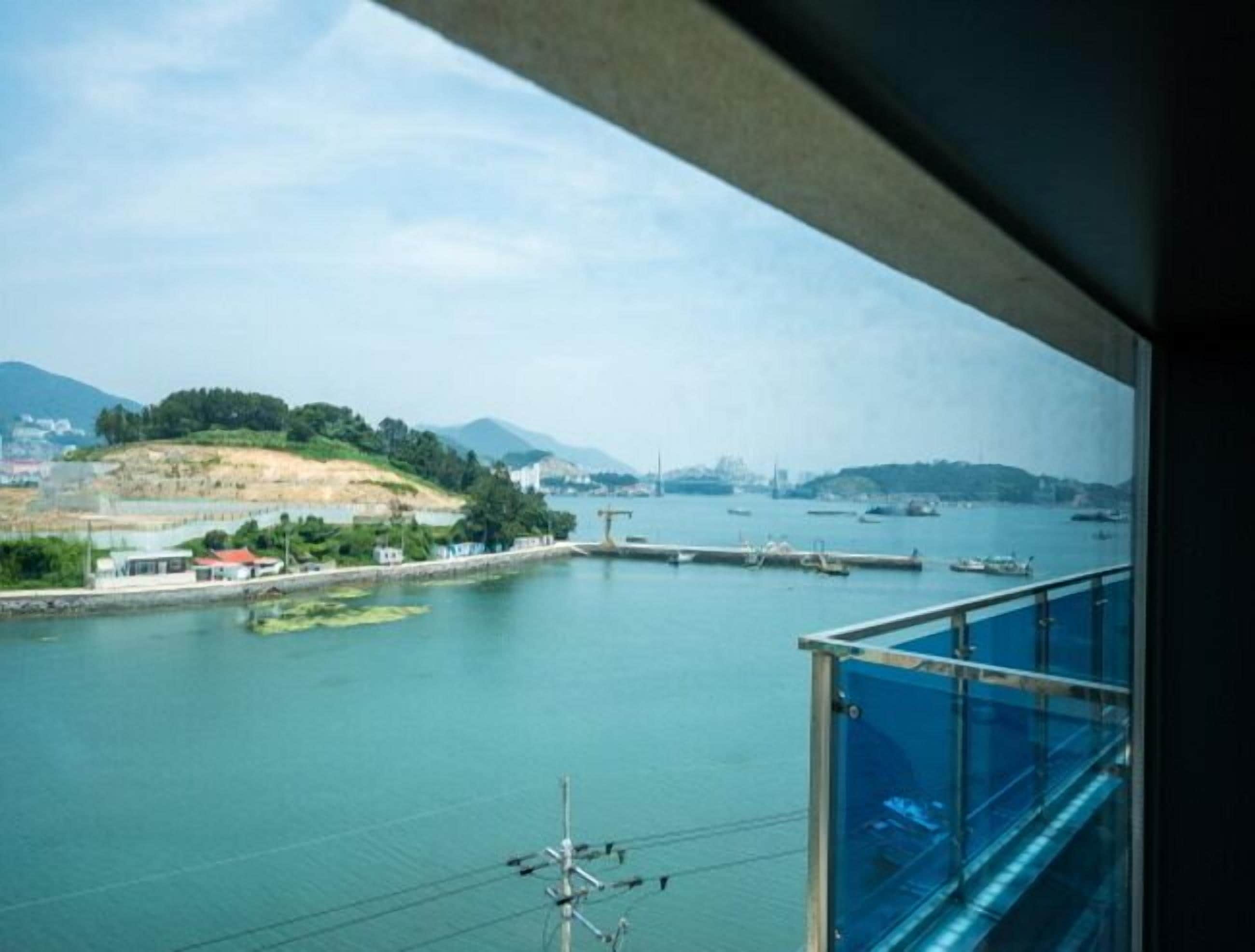 A view from a balcony overlooking a body of water with boats, a dock, and distant buildings.